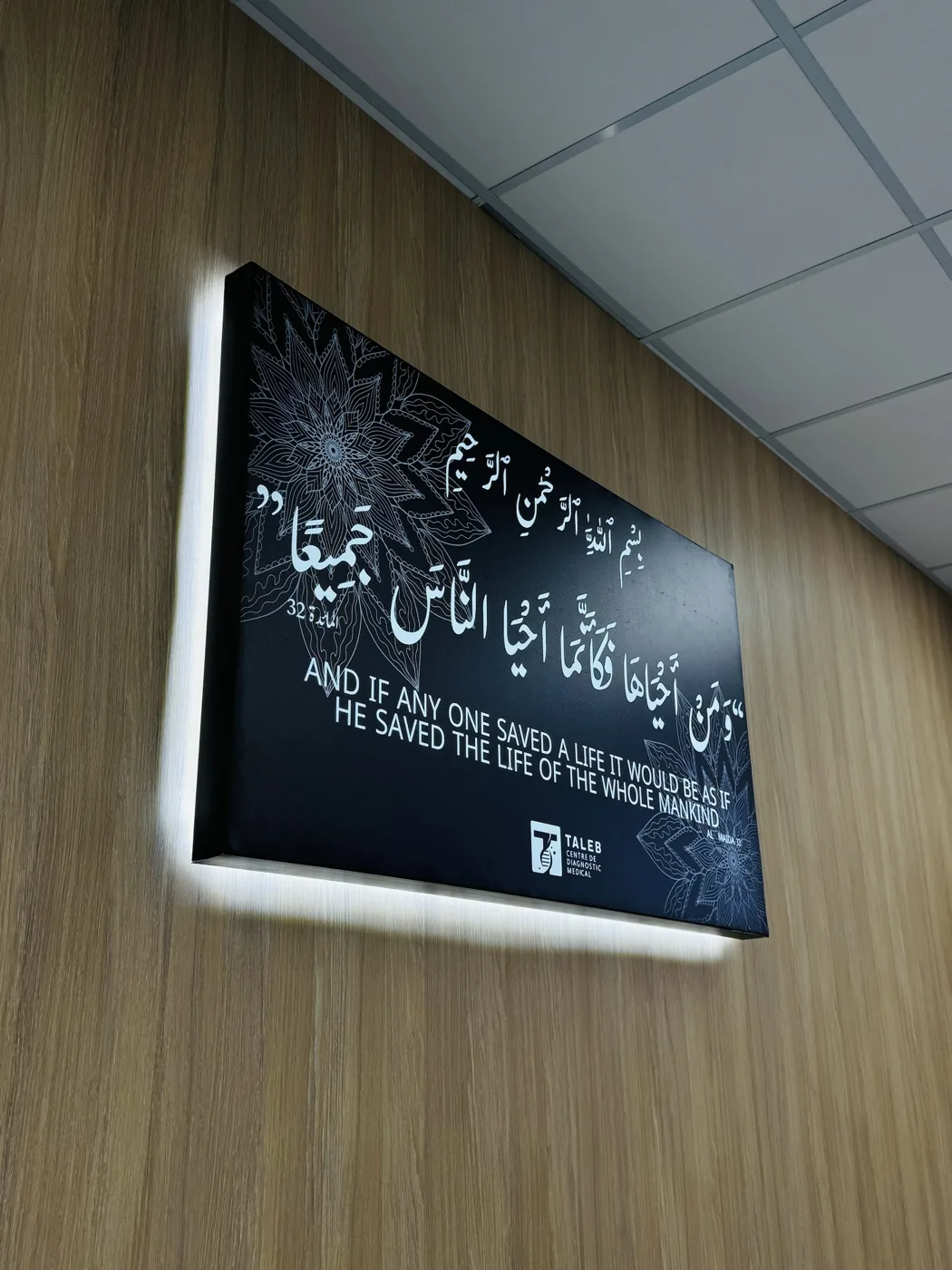 Caisson rétroéclairé avec un verset calligraphié en arabe et sa traduction anglaise, sur un mur en bois